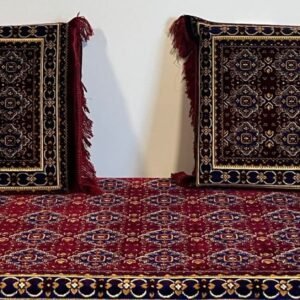 Intricately patterned cushions and carpet with fringe and geometric motifs against a wall.