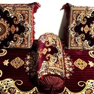 Intricately designed cushions and bolster on a patterned carpet with red and gold motifs.
