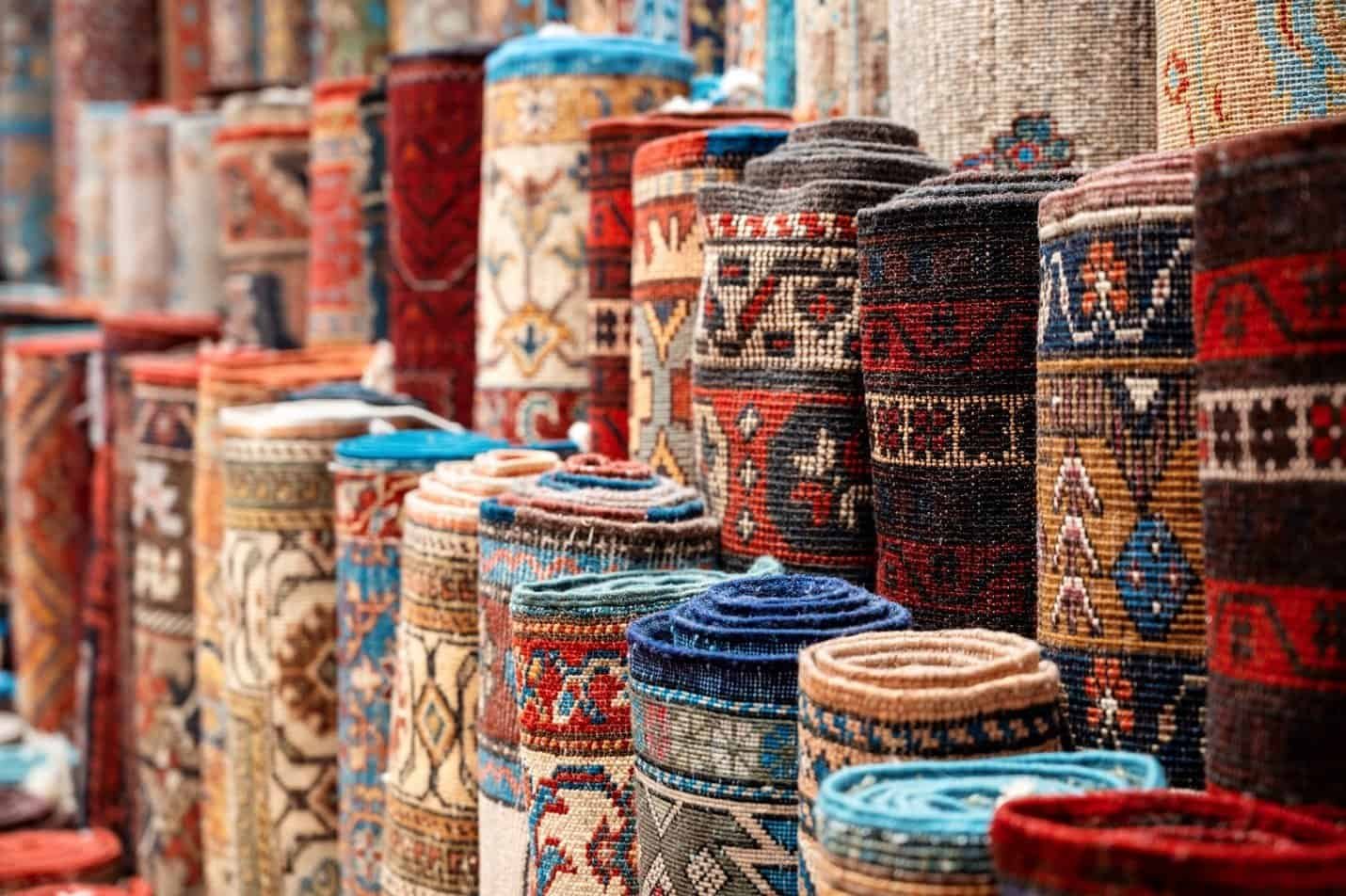 Rolled rugs with intricate patterns in various colors are displayed upright.